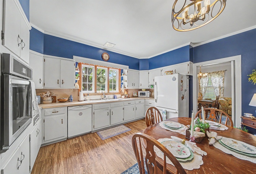 Kitchen with light countertops, white appliances, a chandelier, white cabinets, and crown molding