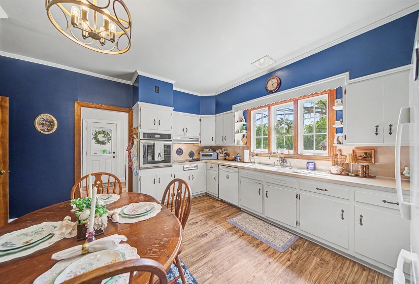 Kitchen featuring light countertops, white appliances, light wood-style floors, crown molding, and suspended lighting