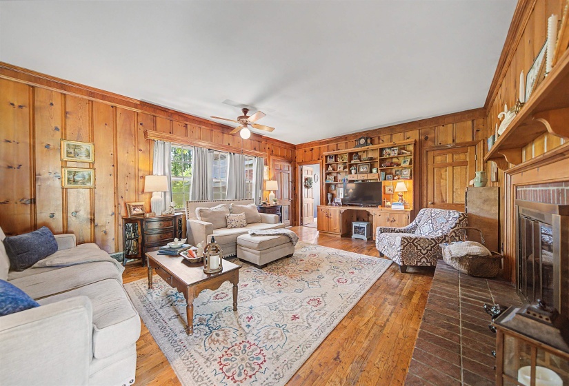 Living room with wood walls, hardwood / wood-style flooring, a glass covered fireplace, and ceiling fan