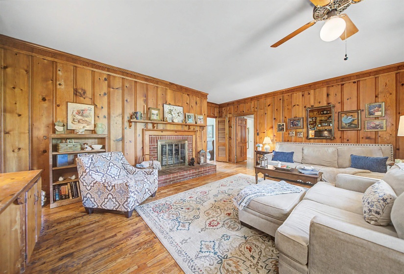 Living room with wooden walls, light wood-style flooring, a brick fireplace, and a ceiling fan