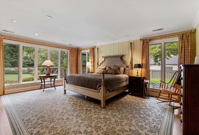 Spacious and Elegant Primary Bedroom Suite Showcasing Gleaming Hardwood Floors, Classic Crown Molding, and a Stunning Wall of Windows That Fill the Room with Natural Light and Offer Serene Views of the Beautifully Landscaped Rear Yd. A Tranquil Retreat.