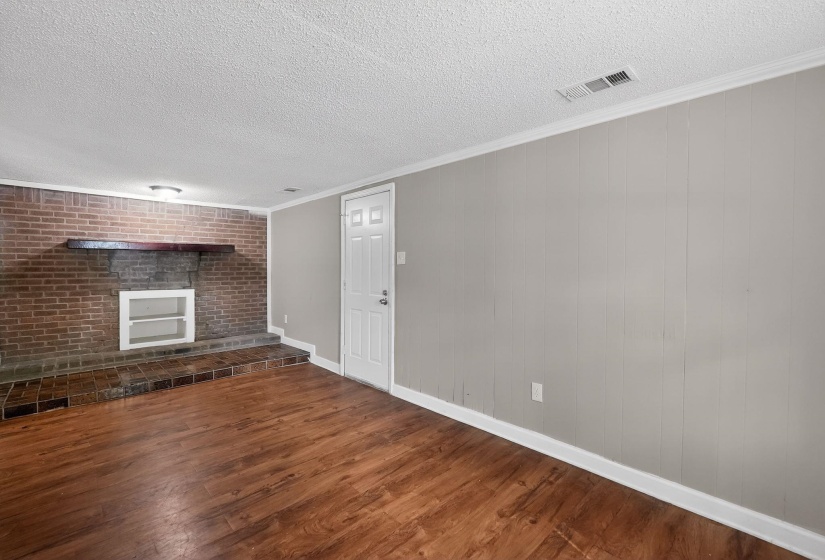 Unfurnished living room featuring a fireplace, dark wood finished floors, crown molding, brick wall, and a textured ceiling