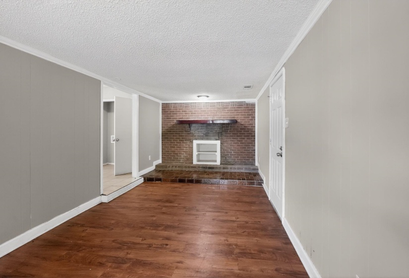 Unfurnished living room featuring ornamental molding, a fireplace, dark wood finished floors, a textured ceiling, and wood walls