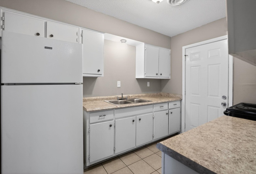 Kitchen with freestanding refrigerator, white cabinetry, light countertops, a textured ceiling, and light tile patterned flooring