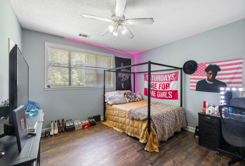 Bedroom featuring wood-finish flooring, a ceiling fan with integrated lighting, and a large window with blinds