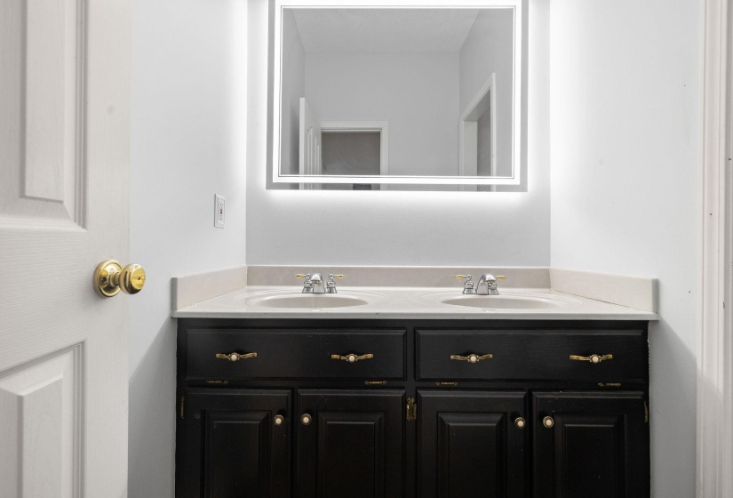 Dual vanity featuring undermount sinks, light-toned countertop, and black cabinetry with gold-toned hardware