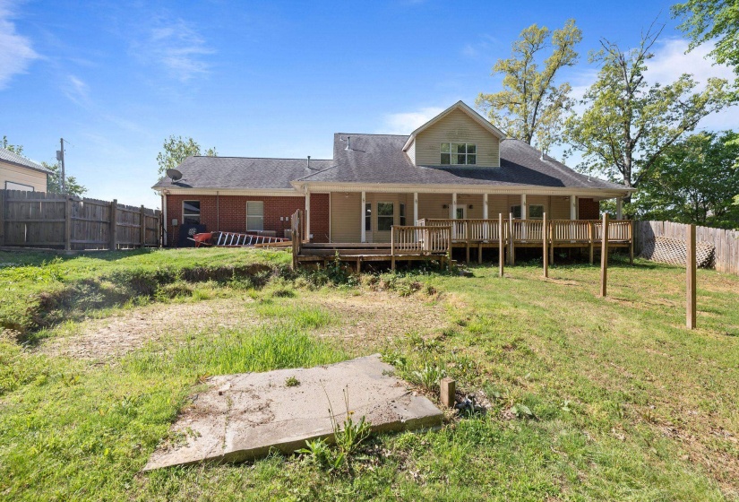 Rear exterior featuring a full-width deck with wooden railings, exposed support posts, and a covered porch area