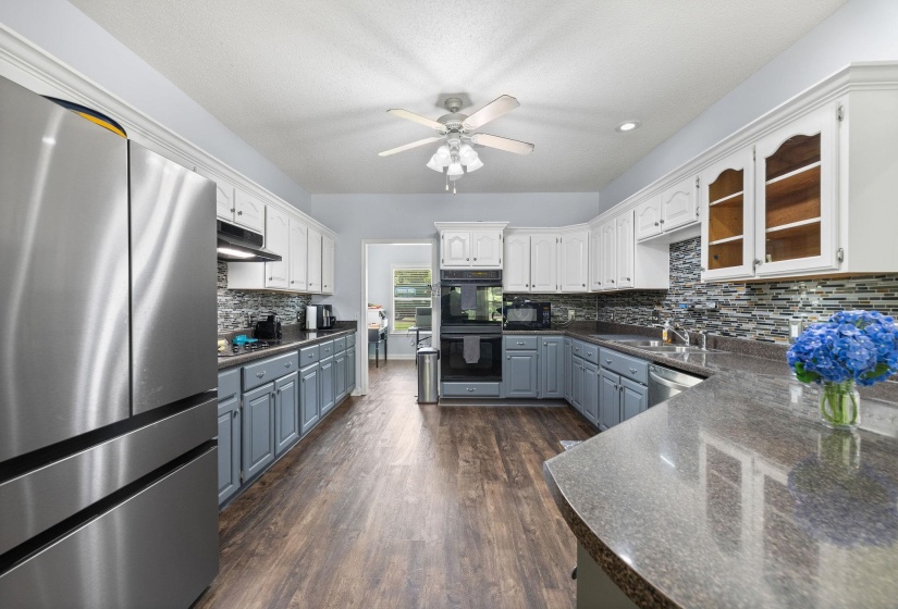 Kitchen featuring dual tone cabinetry, black appliances, dark wood-type flooring, a ceiling fan, and tasteful backsplash