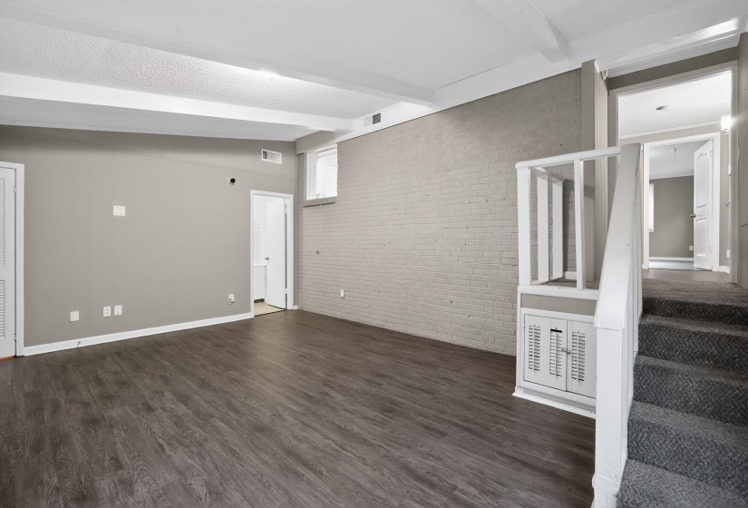 Empty room with brick wall, dark wood finished floors, and lofted ceiling with beams