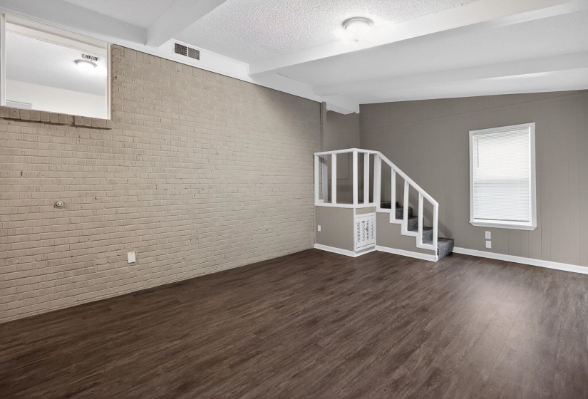 Unfurnished living room with brick wall, beamed ceiling, and dark wood-style flooring