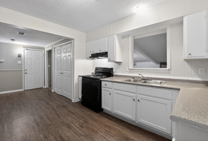 Kitchen with a textured ceiling, black electric range, white cabinetry, light countertops, and dark wood-type flooring