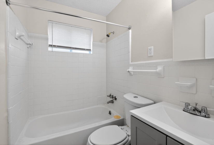 Full bath with vanity, a textured ceiling, washtub / shower combination, tile walls, and a wainscoted wall