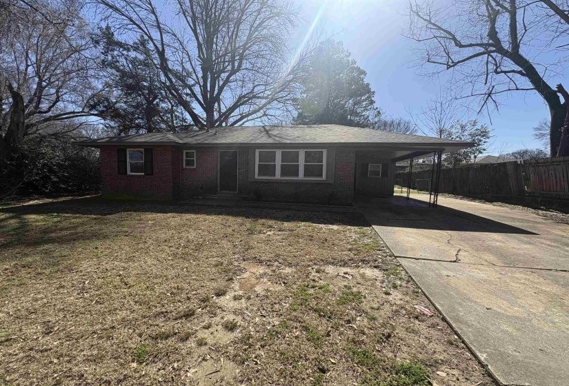 Ranch-style home featuring a carport, driveway, brick siding, and a front yard