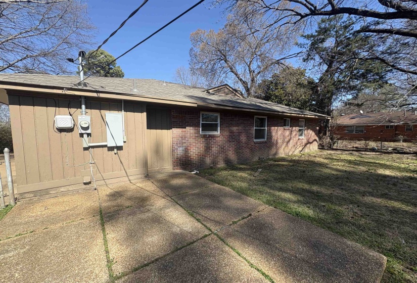 View of property exterior featuring brick siding, roof with shingles, a patio, and a lawn