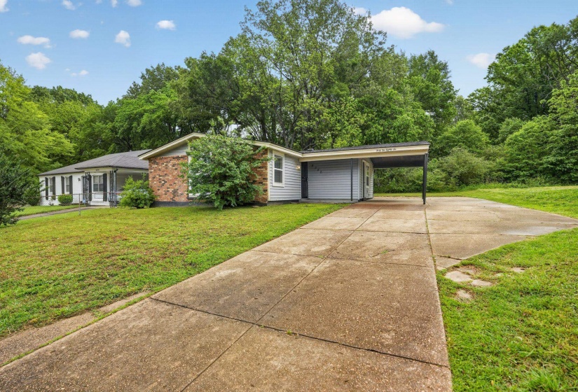 View of front facade with a front yard, concrete driveway, an attached carport, and brick siding