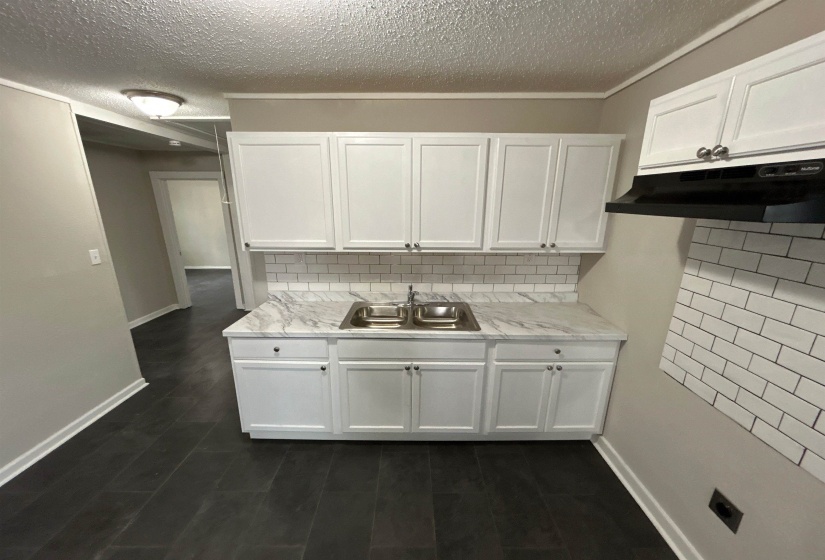 Kitchen featuring light countertops, backsplash, white cabinets, and a textured ceiling