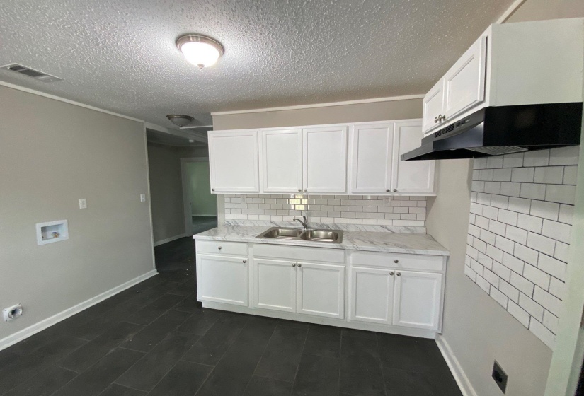 Kitchen featuring light countertops, white cabinets, a textured ceiling, crown molding, and decorative backsplash