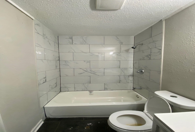 Bathroom featuring a textured wall, vanity, a textured ceiling, shower / bathtub combination, and dark tile patterned flooring