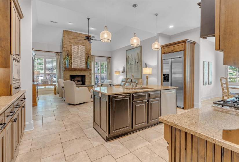 Kitchen featuring light stone countertops, open floor plan, a kitchen island with sink, hanging light fixtures, and built in appliances
