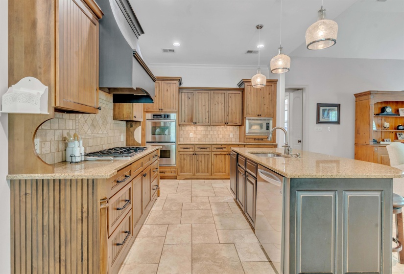Kitchen featuring light stone counters, stainless steel appliances, a center island with sink, decorative light fixtures, and crown molding