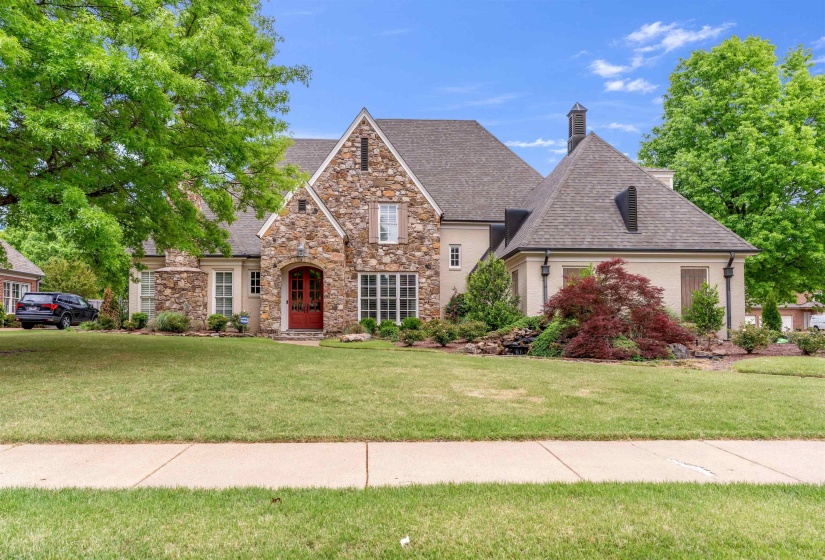 View of front facade featuring a front lawn, stone siding, a chimney, and a shingled roof
