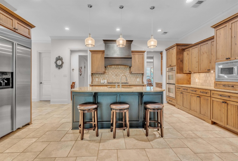 Kitchen featuring light stone counters, built in appliances, decorative light fixtures, a breakfast bar, and an island with sink