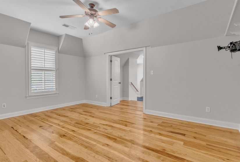 Empty room featuring a ceiling fan, vaulted ceiling, and light wood finished floors