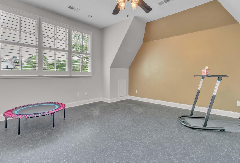 Room with grey carpeting, three large windows featuring white plantation shutters, and a sloped ceiling