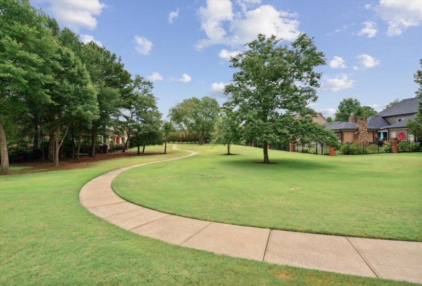 Expansive green space featuring a winding concrete pathway, mature trees, and manicured lawn