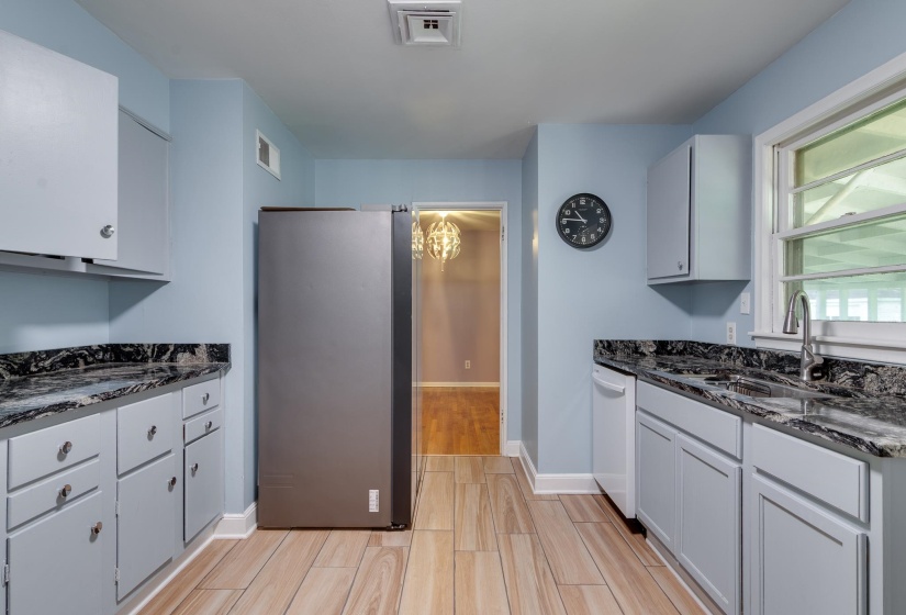 Kitchen featuring wood-finish flooring, a stainless steel refrigerator, white cabinetry, dark countertops, and a window above the sink