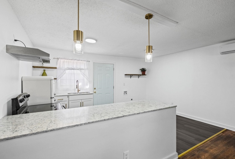Kitchen featuring a peninsula with a light-toned countertop, white cabinetry, a stainless steel range hood, and pendant lighting