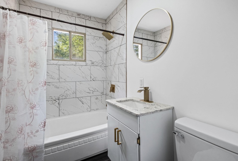 Bathroom featuring a white bathtub with subway tile surround, a window, and a white vanity with a light-toned countertop