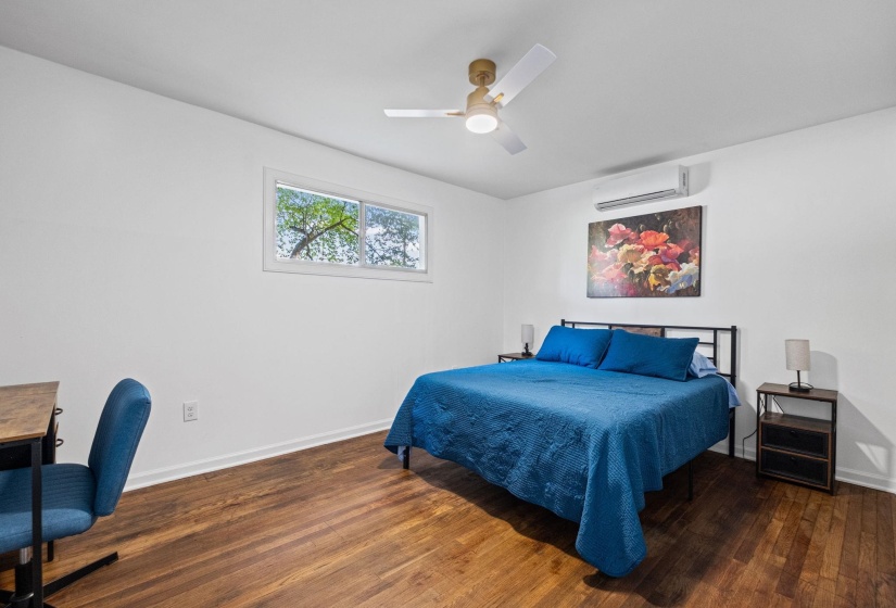 Spacious room featuring wood-finish flooring, a ceiling fan with integrated lighting, and a wall-mounted climate control unit