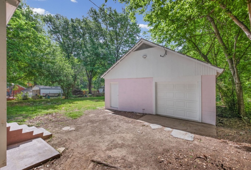 Detached garage with a paneled door, side entrance, and light-colored siding