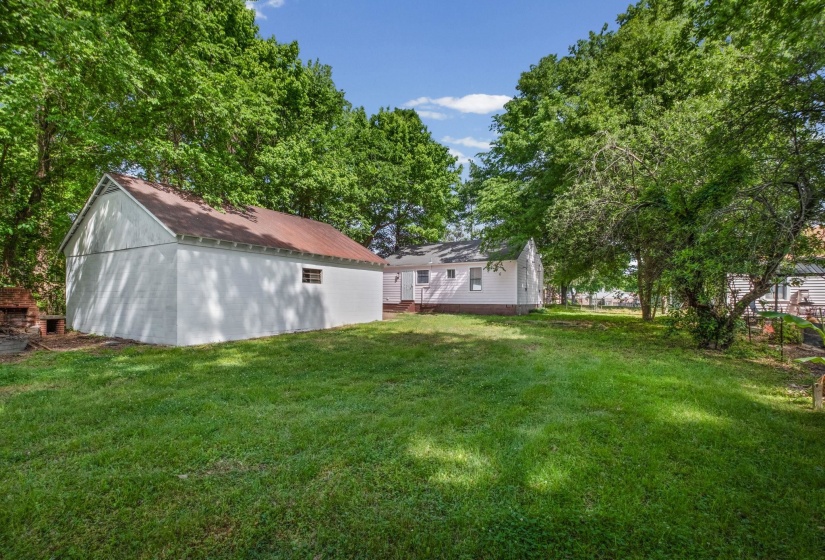 Spacious backyard featuring a white outbuilding with a brown roof, a red brick outdoor oven, and a secondary white structure