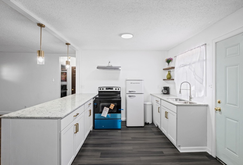 Kitchen featuring a long island with a light-toned countertop, white cabinetry with gold-toned hardware, dark wood-finish flooring, and pendant lighting