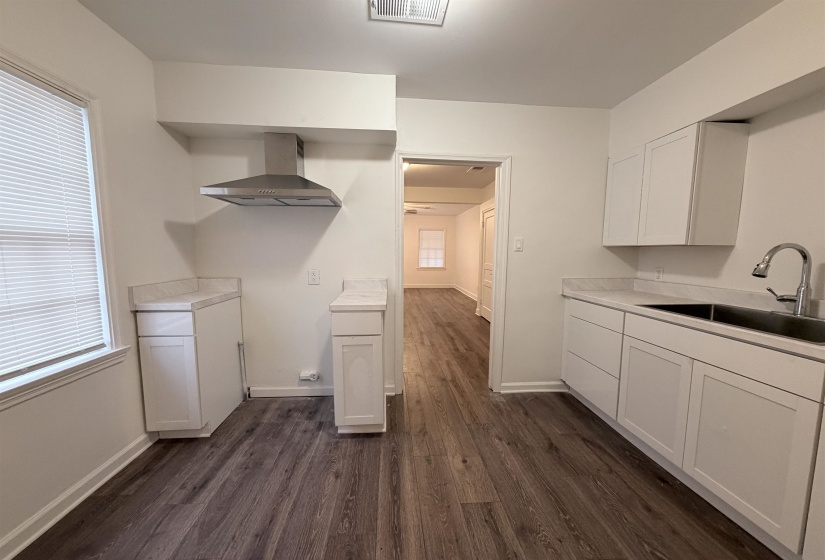 Kitchen with white cabinetry, light countertops, wall chimney range hood, and plenty of natural light