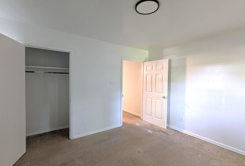 Room featuring white painted walls, a flush-mount ceiling light, a white paneled door, a closet with a built-in shelf and hanging rod, and baseboard trim