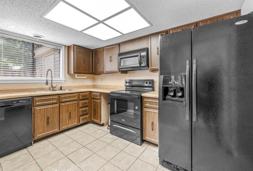 Kitchen featuring wood-finish cabinetry, black appliances, a tile floor, and a window with blinds