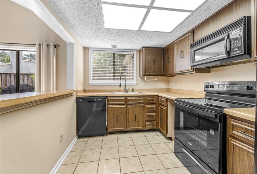 Functional kitchen featuring wood-finish cabinetry, tile flooring, and integrated black appliances