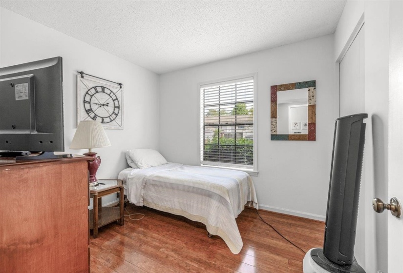 Bedroom featuring wood-finish flooring, white walls, and a window with horizontal blinds