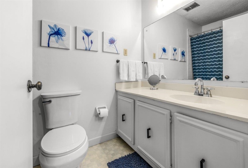 Bathroom featuring a single-sink vanity with white cabinetry, a built-in mirror, a toilet, a shower with a patterned curtain, and light-colored flooring