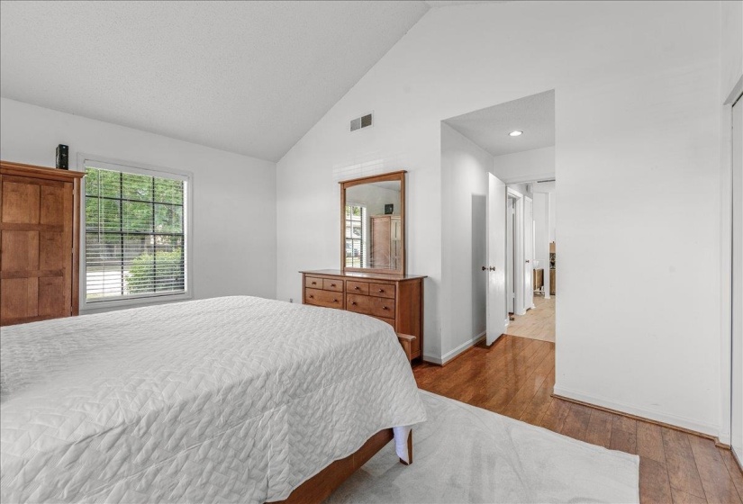 Spacious interior featuring a vaulted ceiling, wood-finish flooring, and a large window with blinds