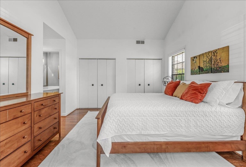 Bedroom featuring vaulted ceilings, wood-finish flooring, and multiple closet storage options