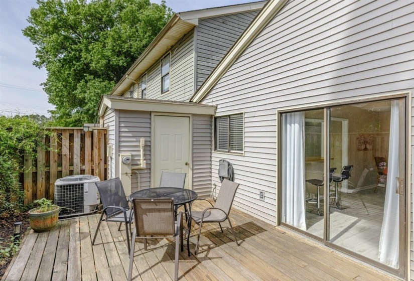 Spacious outdoor deck with sliding glass door access to the interior, exterior siding, and a privacy fence