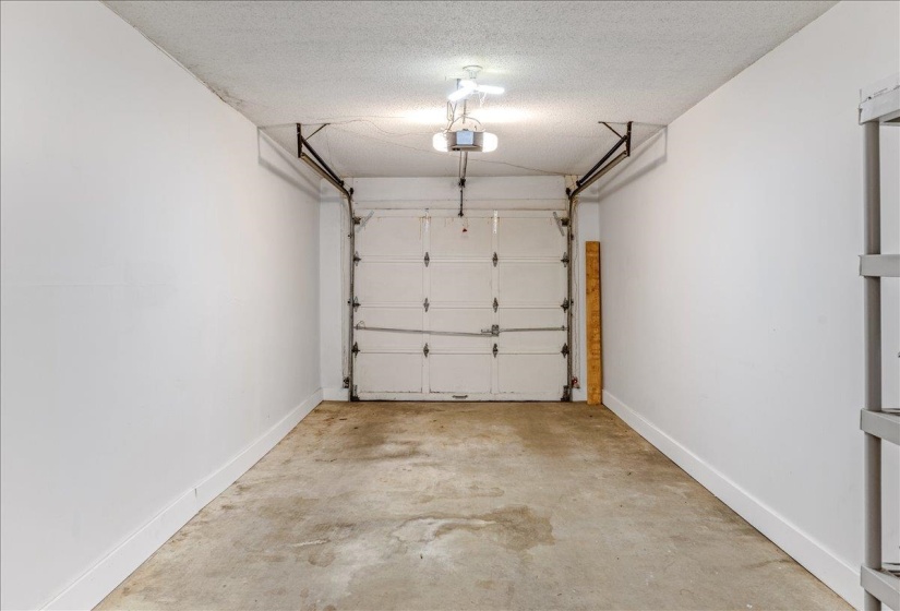 Spacious garage featuring a sectional garage door, exposed ceiling joists, and concrete flooring