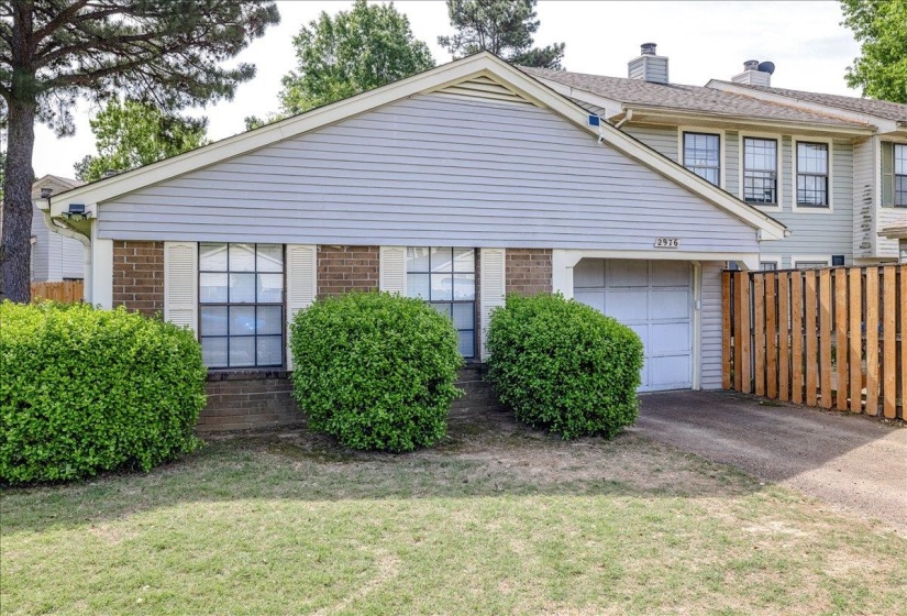 Front exterior featuring brick accents, horizontal siding, an attached garage, a driveway, and mature landscaping