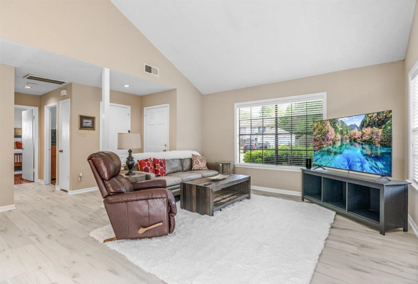 Spacious living area featuring vaulted ceilings, light-tone wood-finish flooring, and multiple entryways