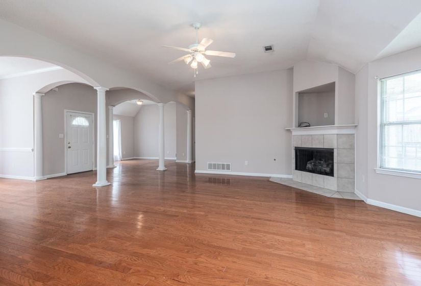 Spacious interior featuring wood-finish flooring, a ceiling fan, and arched room entries with decorative columns