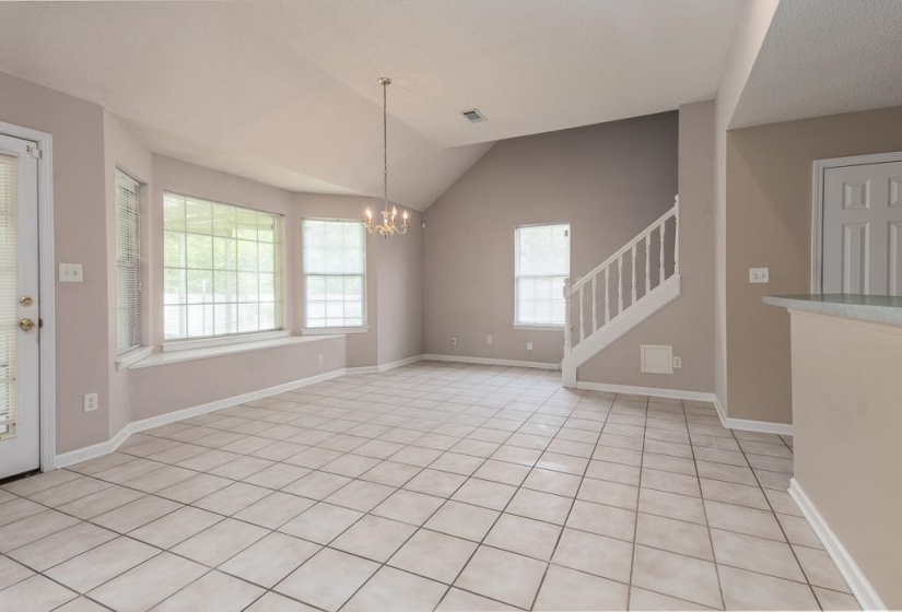 Spacious room featuring vaulted ceilings, a bay window with integrated seating, tile flooring, a staircase with white balusters, and a chandelier